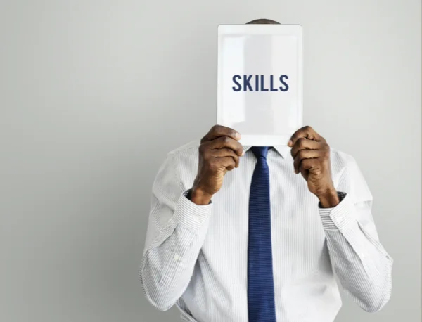 Un homme masque son visage avec une tablette affichant le mot « Skills », pour illustrer le diagnostic des compétences