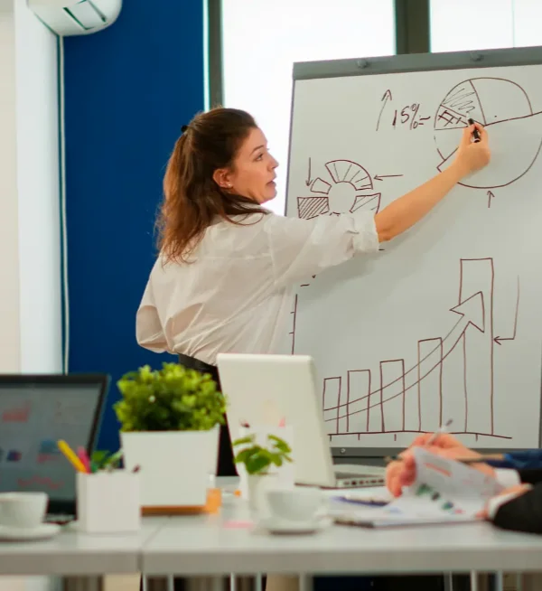Une consultante présente des graphiques de résultats sur un paperboard devant une équipe