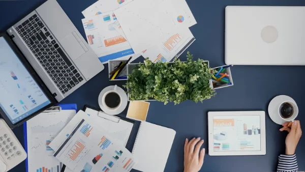 Bureau vu du dessus avec tableaux de bord, graphiques et tablette, pour illustrer la réorganisation de l'activité